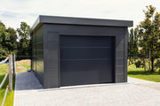A Telluria Garage 3654 in anthracite installed on a block paved driveway, garage door closed, with lawn and mature trees behind it