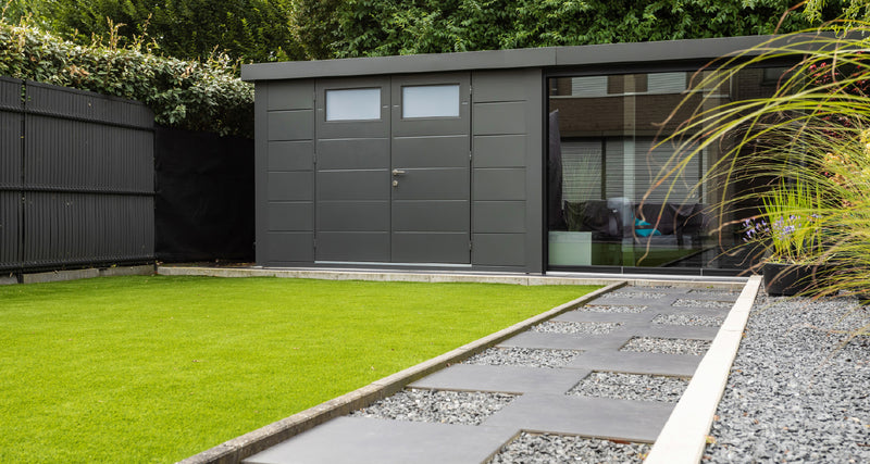 The same Telluria glass sliding door system seen from across a garden, fitted to the open side of a Classico building, showing how the glazed front reads against the steel walls